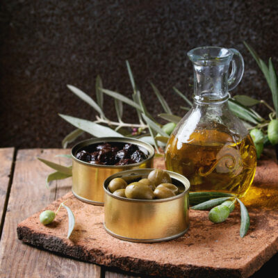 Olives with bread and oil Green and black olives in tin cans, young olives branch and bottle of olive oil on clay board over old wood background. Square image
